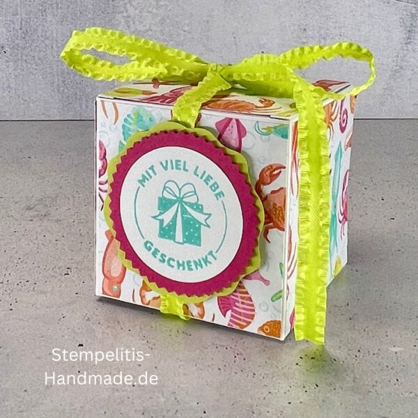 Handdekorierte Geschenkschachtel mit Schleife von oben, Geschenkschachtel mit liebevollem Aufkleber “Mit viel Liebe verschenkt”, Detailansicht Schleife auf Geschenkschachtel, Seitenansicht Geschenkschachtel mit buntem Designpapier, Offene Geschenkbox zum Befüllen, Geschenkschachtel auf hellem Hintergrund mit Dekorband, Handgemachte Geschenkverpackung mit grünem Band und Etikett